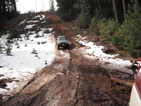 1991 Ford Bronco - An SUV navigates a challenging off-road path with patches of snow and mud.
