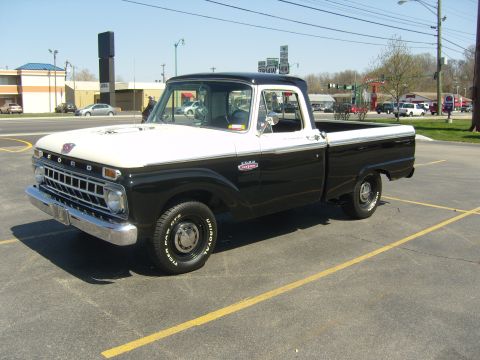 2007 Ford Mustang - Black-over-white mid-1960s Ford F-100 styleside pickup photographed from the driver-side front three-quarter angle in a sunny parking lot.…