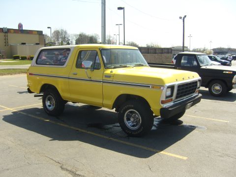2007 Ford Mustang - A yellow 1978 Ford Bronco is parked in a lot next to a black pickup truck.