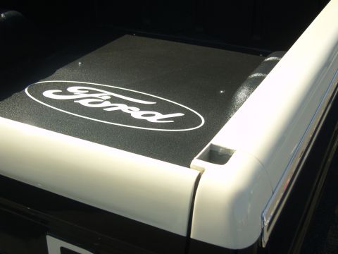 2007 Ford Mustang - Close-up of a Ford oval logo on a black truck bed liner with white bed rails.