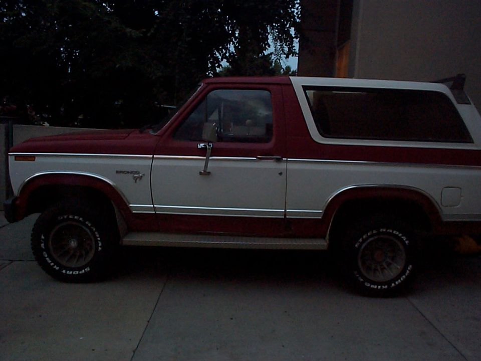 Side view of a two-tone red and white 1980 Ford Bronco with chrome trim and 'Bronco' badging