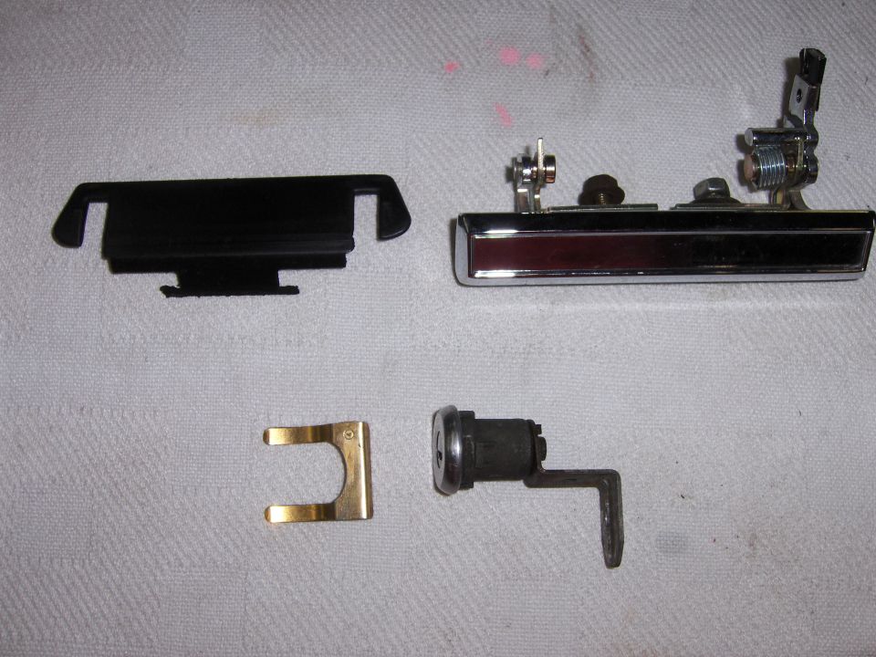 Car door handle assembly, lock cylinder, and trim piece laid out on a white surface