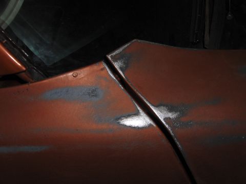 1980 Chevrolet Camaro - Close-up of an orange car's body panel seam, showing areas of primer and exposed metal.
