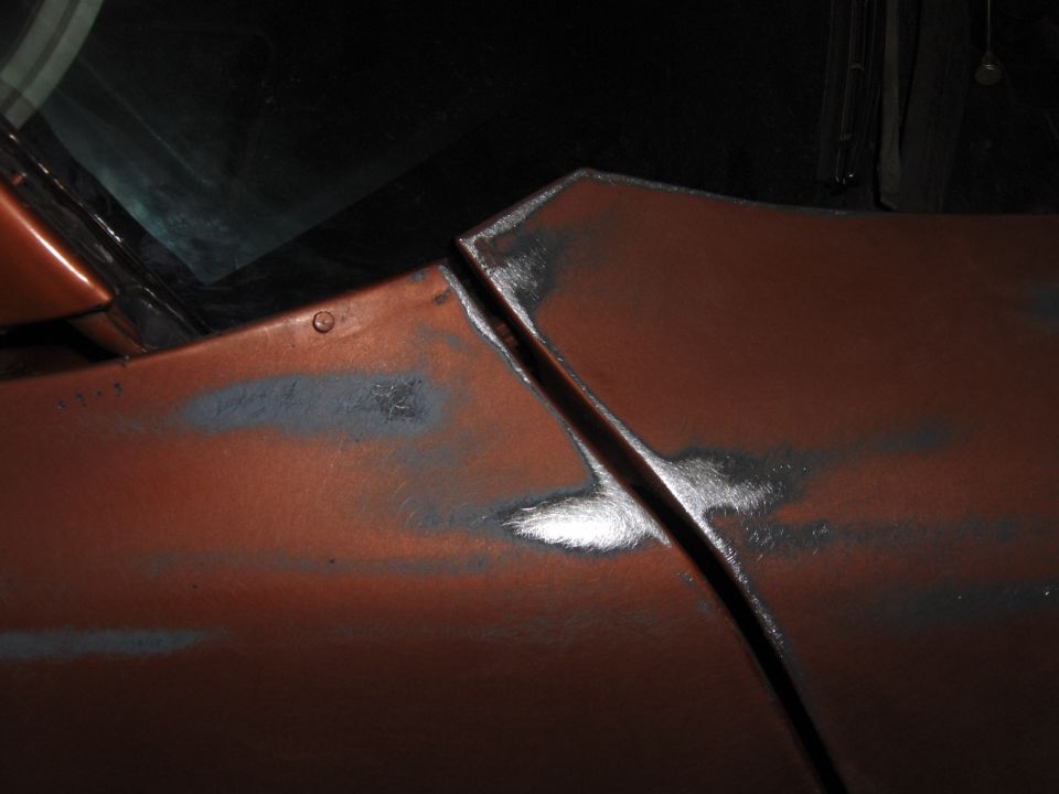Orange car body panel seam with primer patches and visible metal