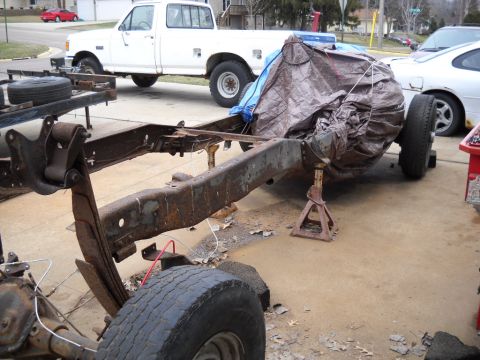 1954 Ford F-100 - A rusty truck chassis is supported by jack stands, with other vehicles visible in the background.