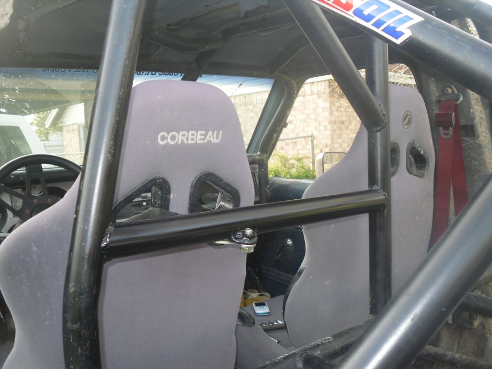 Roll cage inside a vehicle with Corbeau seats and a red racing harness