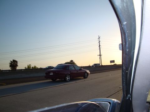 1995 Ford Taurus - A maroon sedan travels down the highway during sunset, with other vehicles visible in the distance.
