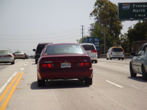 1995 Ford Taurus - A red sedan with a 'TAURUS' badge is seen from behind on a sunny highway with other vehicles.