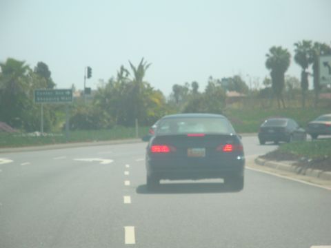 1995 Ford Taurus - A dark sedan drives on a highway, with other vehicles in the distance and a street sign on the left.