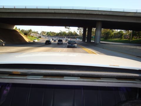 1995 Ford Taurus - Driving on a sunny day under a large concrete overpass with multiple cars on the road ahead.