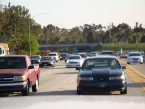 1995 Ford Taurus - A dark 1995 Ford Taurus drives in traffic on a sunny day.