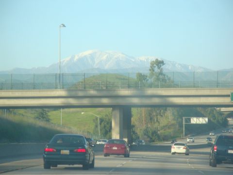 1995 Ford Taurus - A view from a highway shows traffic moving under an overpass with distant snow-capped mountains under a clear blue sky.