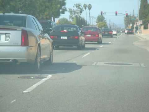 1995 Ford Taurus - Several cars are driving down a street on a clear day, with traffic lights visible in the distance.
