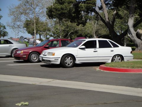 1995 Ford Taurus - Two sedans, a red and a white model, are parked next to each other on a sunny day.