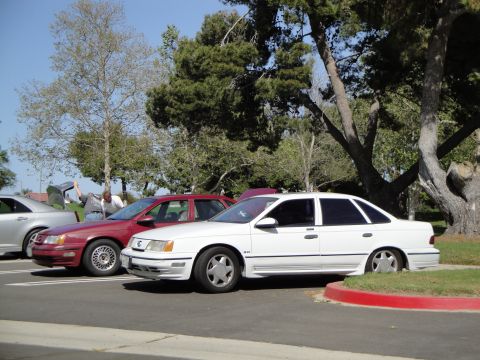 1995 Ford Taurus - A white 1995 Ford Taurus sedan is parked in a lot next to a red sedan.