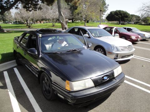 1995 Ford Taurus - A black 1995 Ford Taurus is parked in a lot with other vehicles visible.