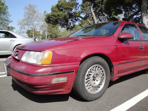 1995 Ford Taurus - A red 1995 Ford Taurus is parked next to another vehicle.