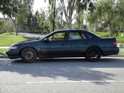 1995 Ford Taurus - A 1995 Ford Taurus sedan is parked on the side of a road, viewed from its left side.