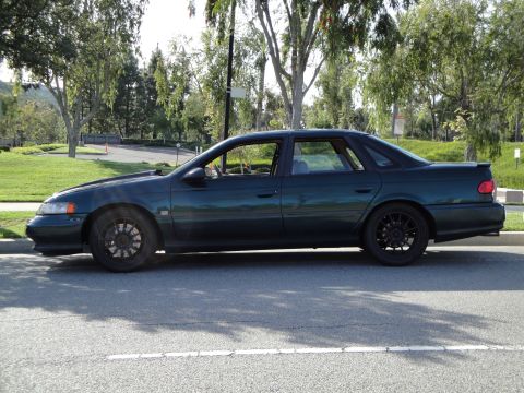 1995 Ford Taurus - Side profile of a dark green 1995 Ford Taurus sedan parked on the side of the road.