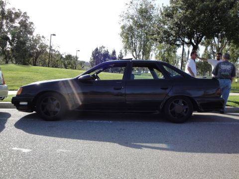 1995 Ford Taurus - Side profile of a dark-colored sedan with a sunroof and aftermarket wheels parked outdoors.