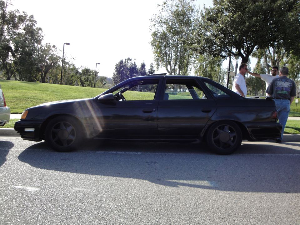 Black sedan parked on asphalt, side view, sun glare on body, aftermarket wheels