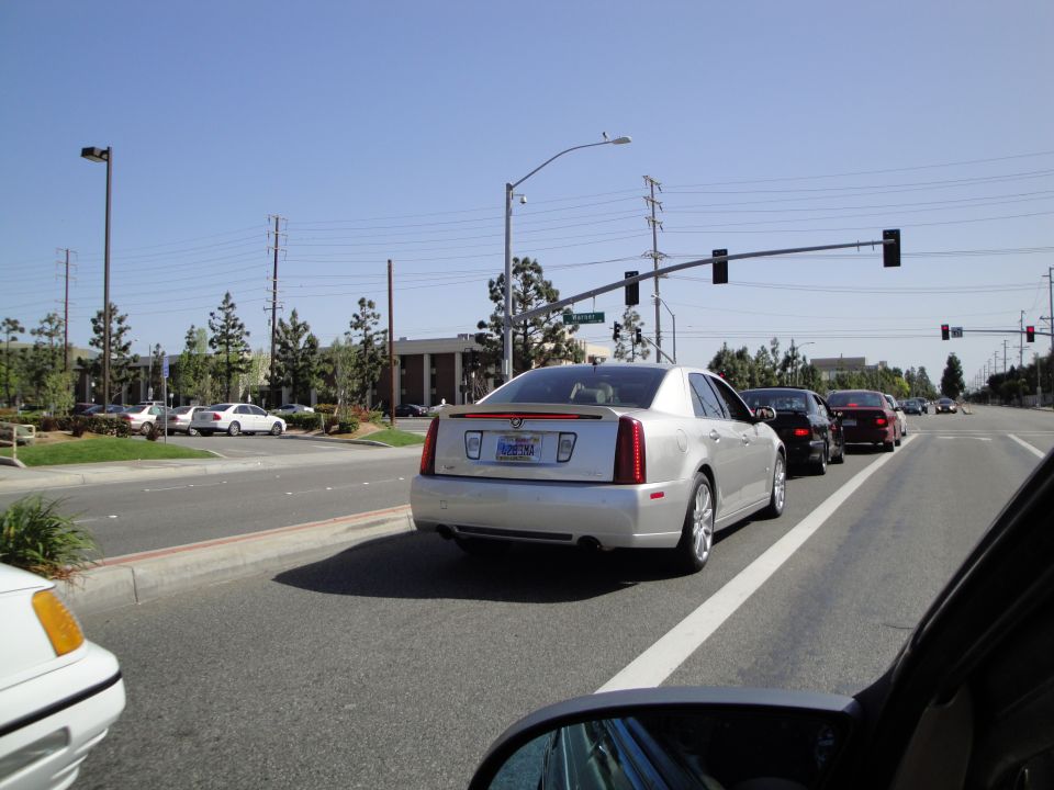 Silver Cadillac sedan in traffic, rear view. License plate is visible