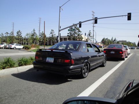 1995 Ford Taurus - A black sedan with a spoiler is seen from the rear, driving in traffic.