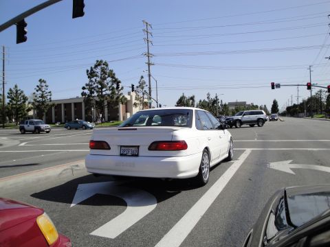 1995 Ford Taurus - A white sedan is seen from behind at a traffic light, with other vehicles in the background.