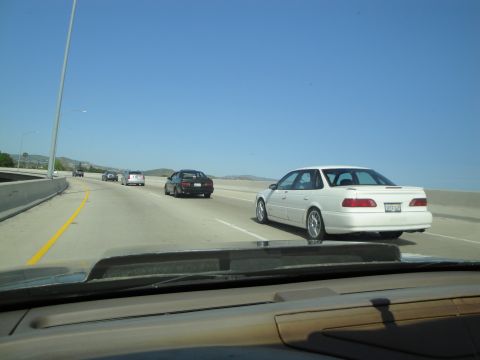 1995 Ford Taurus - Multiple vehicles travel on a highway under a clear blue sky.