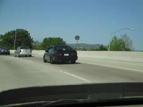 1995 Ford Taurus - A black sedan is seen driving on a highway with other vehicles in the background under a clear blue sky.