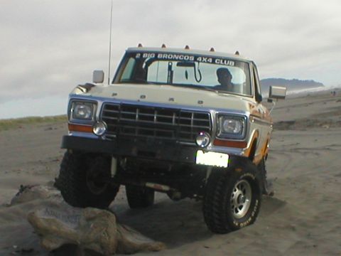 1978 Ford Bronco - 1978 Ford Bronco navigating sandy terrain with one wheel elevated on driftwood.