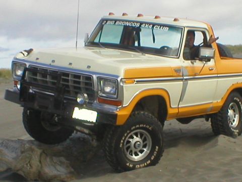 1978 Ford Bronco - This two-tone Ford Bronco is parked on a sandy terrain, possibly a beach, with a prominent bull bar and off-road tires.