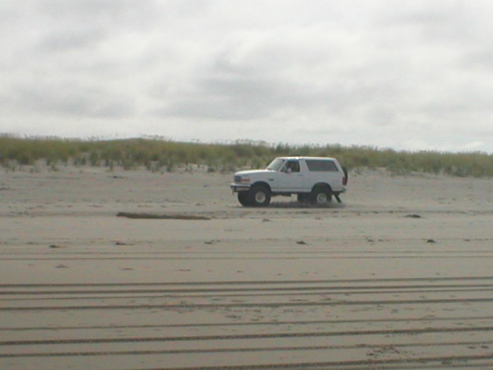 White SUV with spare tire on rear door driving on sand dunes
