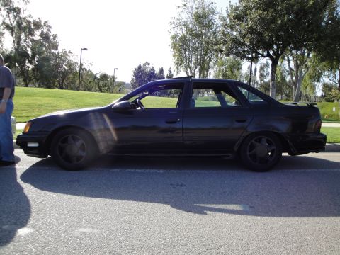 1995 Ford Taurus - The side profile of a black sedan is captured in this outdoor photograph, with a person standing near the front.