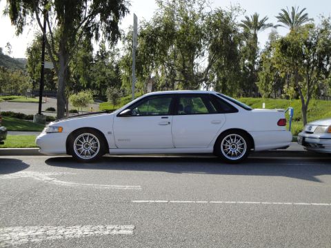 1995 Ford Taurus - A white 1995 Ford Taurus sedan is parked on the side of the road, aftermarket wheels and a rear spoiler.