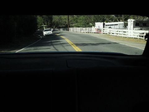 1995 Ford Taurus - A white sedan is seen driving on a road bordered by a white fence and horse trailers.
