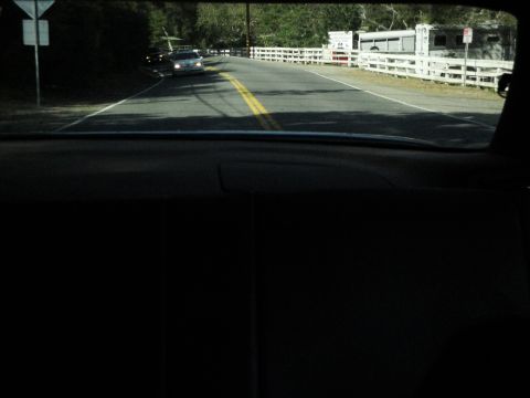 1995 Ford Taurus - A silver sedan is seen from inside a vehicle, driving on a road with a white fence and trailer.