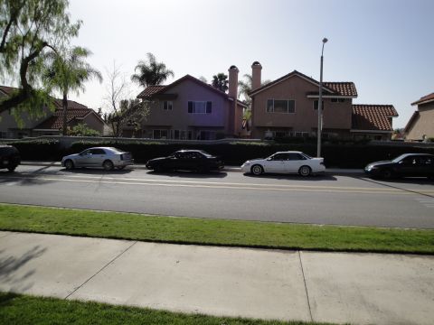 1995 Ford Taurus - Several cars are parked along the curb in front of houses on a sunny day.
