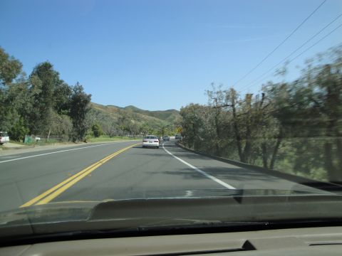 1995 Ford Taurus - A white sedan travels down a highway surrounded by trees and hills under a clear blue sky.