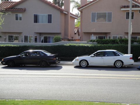 1995 Ford Taurus - Two sedans are parked on the side of a residential street.