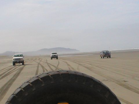 1978 Ford Bronco - Multiple SUVs drive along a sandy beach, leaving tire tracks behind them.