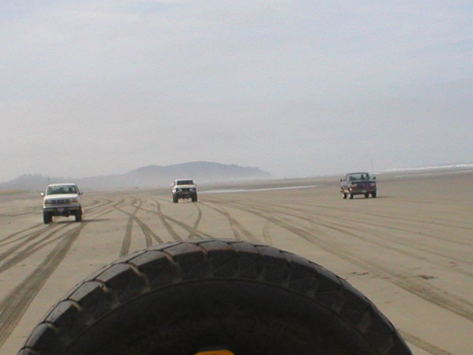 Three SUVs driving on a beach with tire tracks in the sand