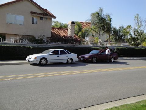 1995 Ford Taurus - A white 1995 Ford Taurus sedan is parked on the street next to a maroon car.