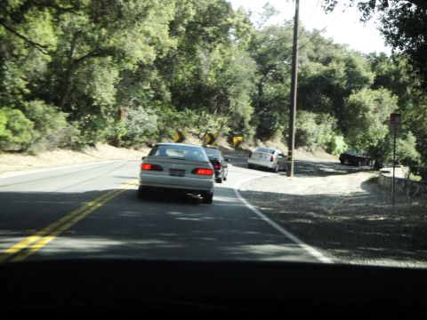 1995 Ford Taurus - A silver 1995 Ford Taurus sedan is seen from behind on a winding road, with other vehicles ahead.