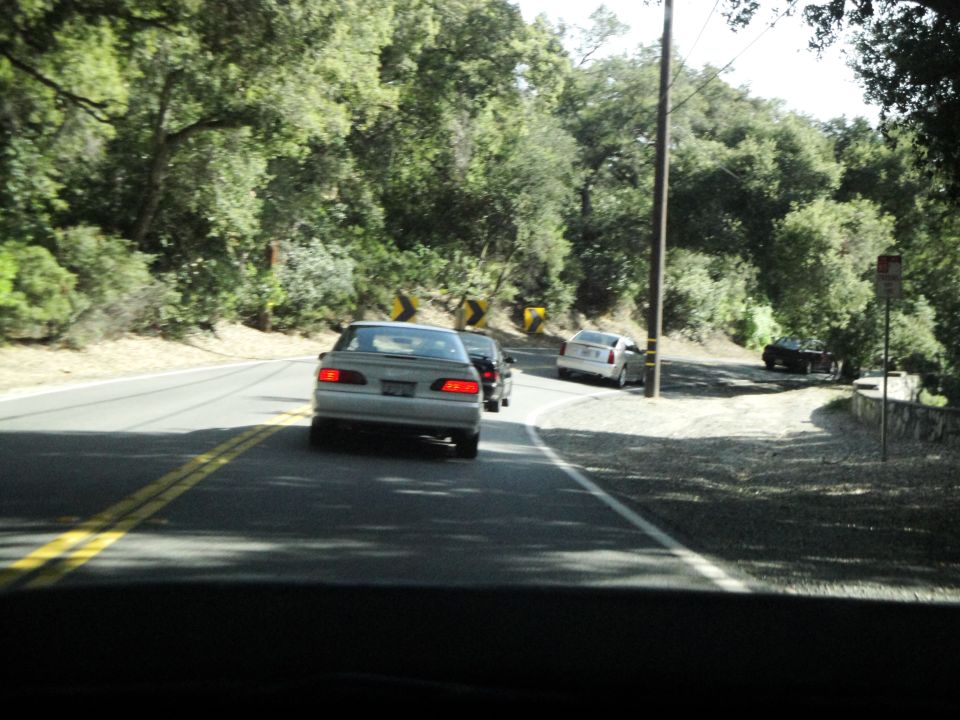 Silver 1995 Ford Taurus sedan, rear view, driving on a two-lane road with trees