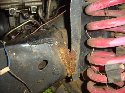 1986 Ford Bronco - Close-up view of a rusted frame section and a pink coil spring, indicating potential structural wear.