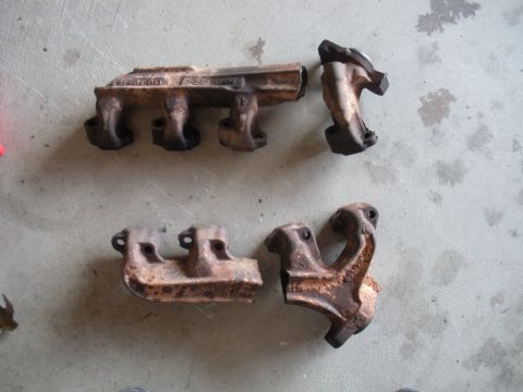 1990 Ford Bronco - Four used exhaust manifolds are laid out on a concrete surface, showing signs of rust and wear.