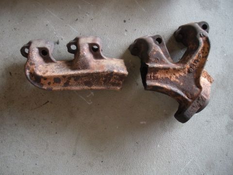 1990 Ford Bronco - Pair of old, rusted exhaust manifolds sit on a gray surface. Part numbers are visible on one.