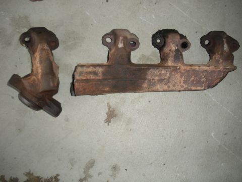 1990 Ford Bronco - Two heavily rusted exhaust manifolds are laid out on a concrete surface, showing signs of wear and age.