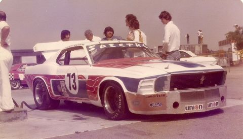 1973 Ford Mustang - A modified race car with racing stripes and a prominent spoiler is being attended to by a crew.
